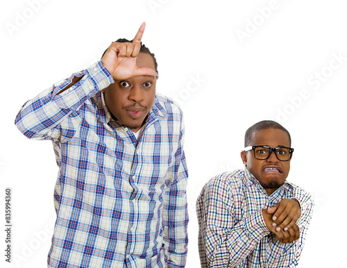 Bild auf Leinwand Portrait two young men, rude bully standing upfront showing looser sign, shy little nerd guy wearing glasses standing anxiously isolated white background