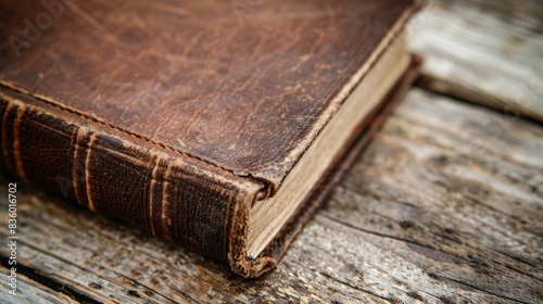 A close-up photograph of a vintage leatherbound book resting on a worn wooden surface. The image captures the texture of the leather and the aged wood