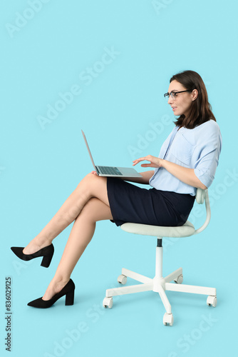 Young businesswoman with laptop sitting on chair against blue background