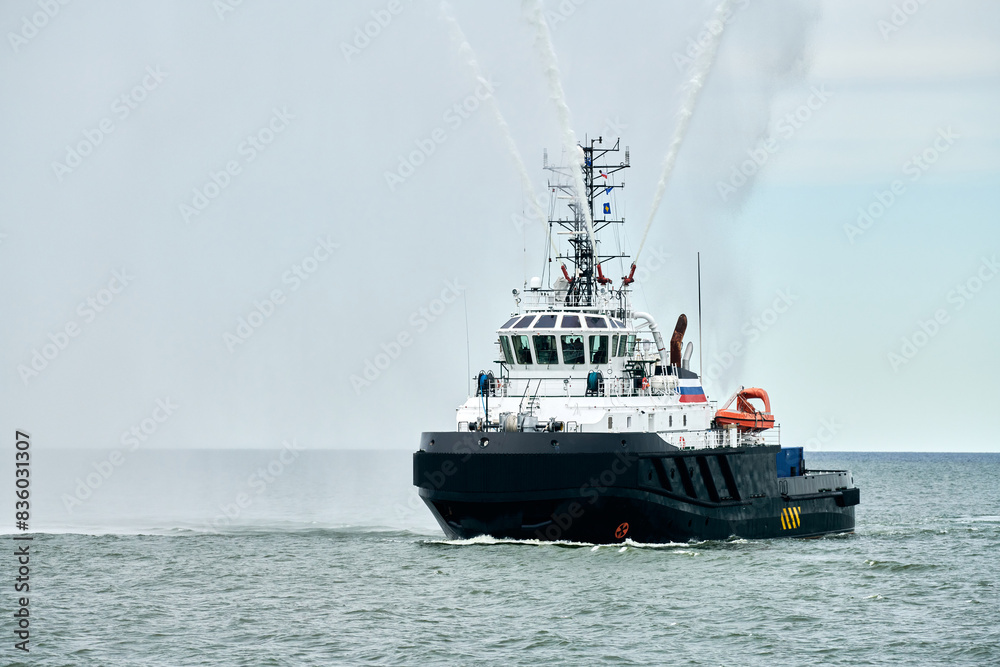 Fireboat ship sails on open sea directing jets of water to sides demonstrating bravery water salute, nautical spectacle of russian maritime strength at Russian naval forces parade Fireboat ship sails on open sea directing jets of water to sides demonstrating bravery water salute, nautical spectacle of russian maritime strength at Russian naval forces parade