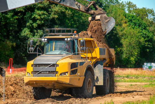 Excavator loading big yellow articulated dump truck earth mover on building site