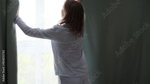 Back view, woman closes blackout curtains in the bedroom for a good sleeping.