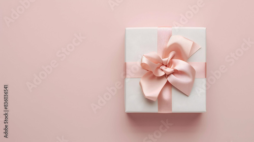Elegant white gift box adorned with a pink satin ribbon, set against a soft pink background. Perfect for celebrations, holidays, or special occasions © Supawee