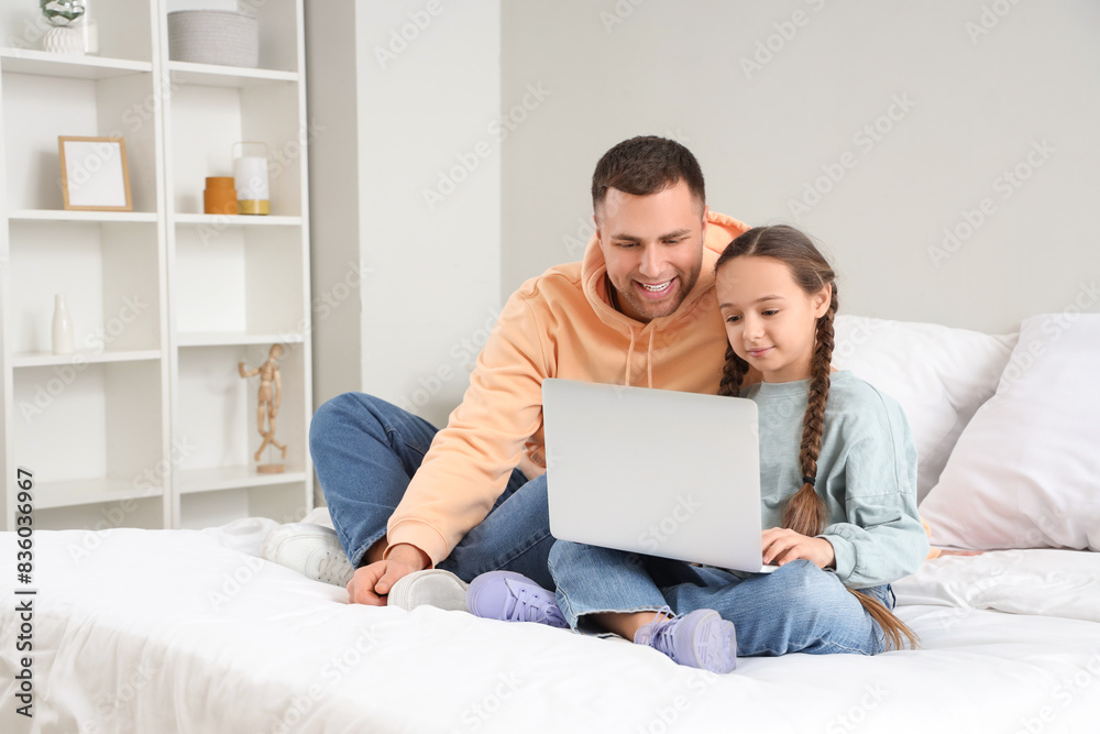 Father and his daughter watching something on laptop together in bedroom Father and his daughter watching something on laptop together in bedroom