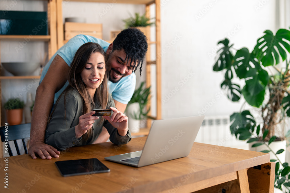 Young happy couple using laptop and credit card while shopping on the internet at home. Young happy couple using laptop and credit card while shopping on the internet at home.