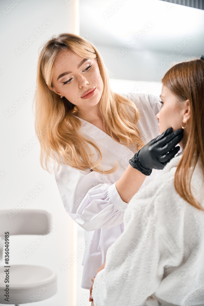 Focused female beautician examining and touching face of young caucasian woman Focused female beautician examining and touching face of young caucasian woman