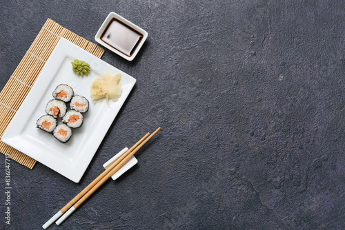 Tasty sushi rolls with soy sauce, chopsticks and bamboo mat on black grunge background