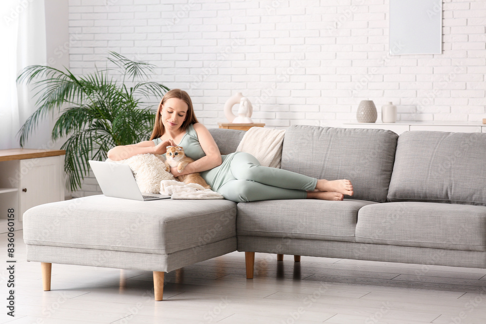 Young woman with cute kitten and laptop lying on sofa at home Young woman with cute kitten and laptop lying on sofa at home