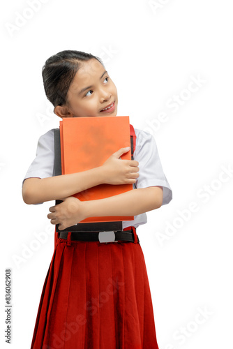 Pensive asian schoolgirl in white shirt and red skirt holding textbook and looking away. Showcasing concentration and curiosity. Isolated on white background