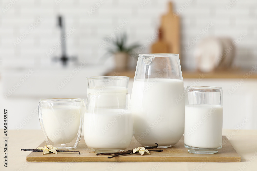Glasses and jug of fresh vanilla milk with sticks and flowers on table in kitchen Glasses and jug of fresh vanilla milk with sticks and flowers on table in kitchen