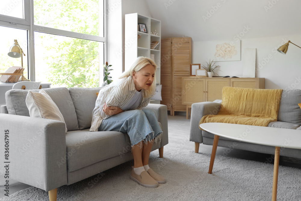 Mature woman suffering from menstrual pain on sofa at home Mature woman suffering from menstrual pain on sofa at home