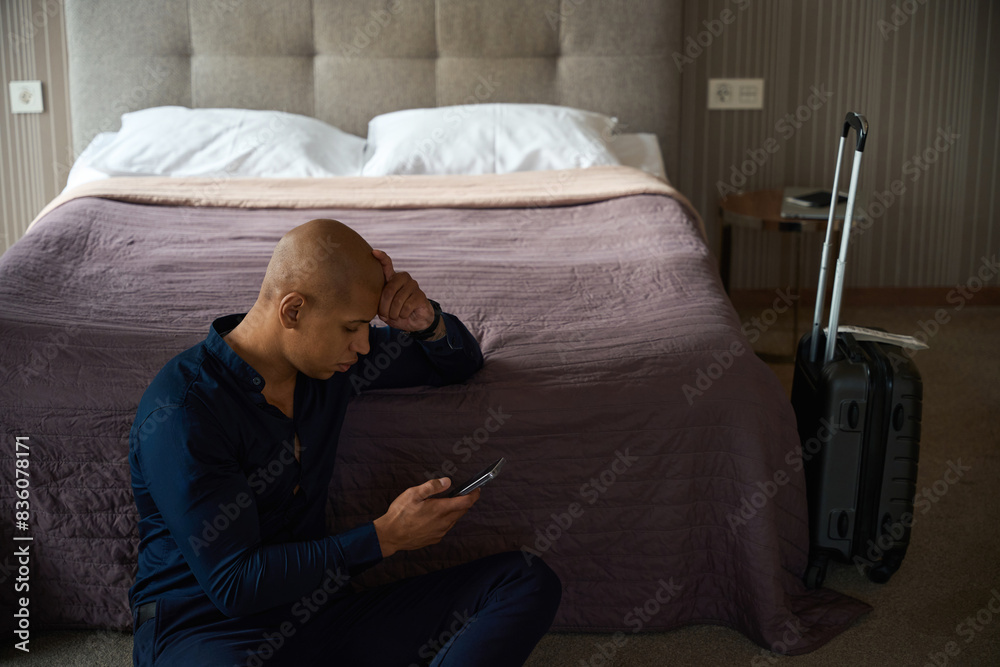 Obraz premium African american businessman watching and using smartphone on floor by bed
