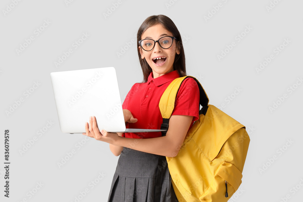 Little schoolgirl in eyeglasses using laptop on light background Little schoolgirl in eyeglasses using laptop on light background