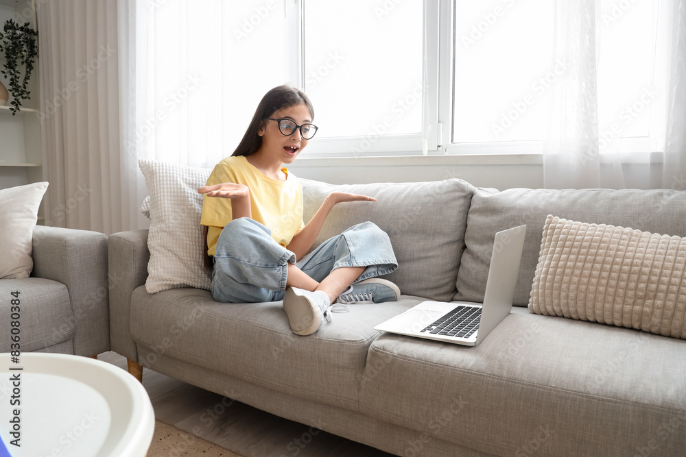 Little schoolgirl in eyeglasses with laptop video chatting on sofa at home Little schoolgirl in eyeglasses with laptop video chatting on sofa at home