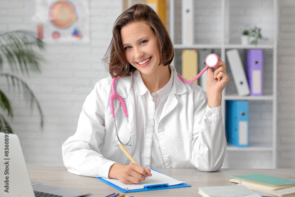 Beautiful female doctor with clipboard and stethoscope at table in clinic Beautiful female doctor with clipboard and stethoscope at table in clinic