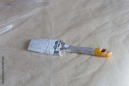 Obraz na płótnie Close-up photo of a wall brush stained with white paint on a bed covered with pl