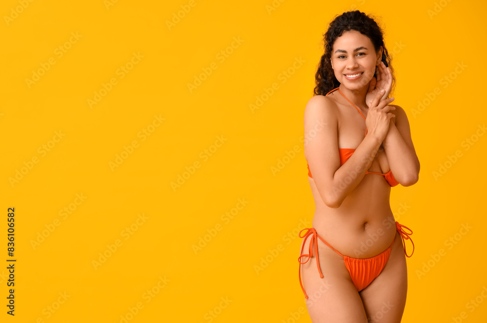 Beautiful young African-American woman in stylish orange swimsuit on yellow background Beautiful young African-American woman in stylish orange swimsuit on yellow background