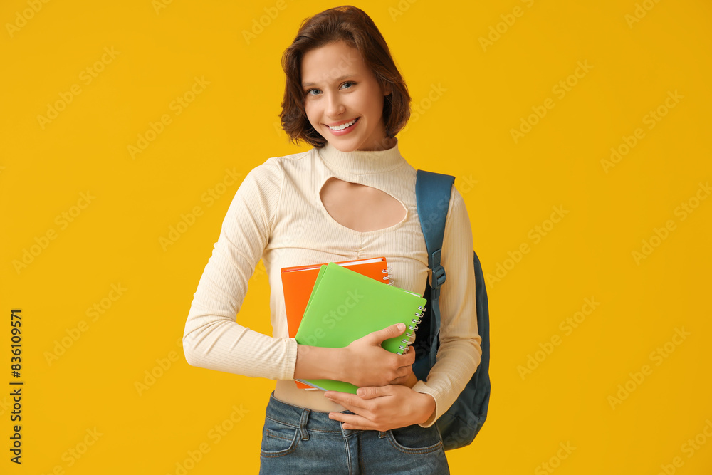 Beautiful female student with notebooks and backpack on yellow background Beautiful female student with notebooks and backpack on yellow background
