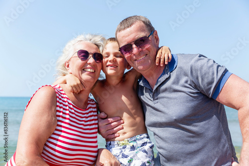 An elderly man and woman hugging a boy on the seashore on a sunny day. Love and tenderness. Happy grandparents with their grandson on vacation.