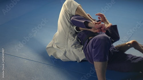 Martial arts athlete in white uniform pulling and throwing his opponent down on mat and doing chokehold during jujutsu practice