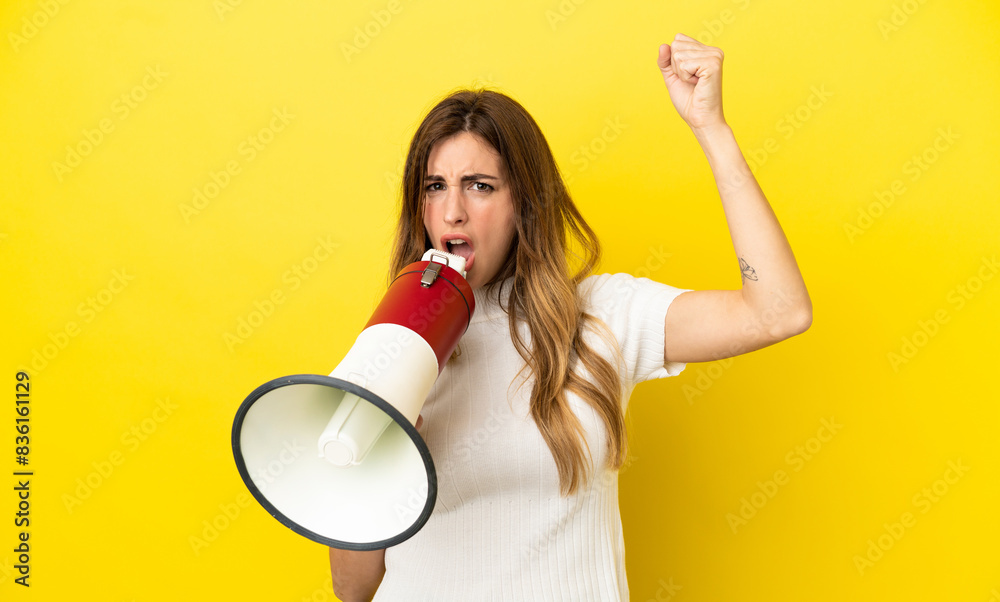 Caucasian woman isolated on yellow background shouting through a megaphone to announce something Caucasian woman isolated on yellow background shouting through a megaphone to announce something