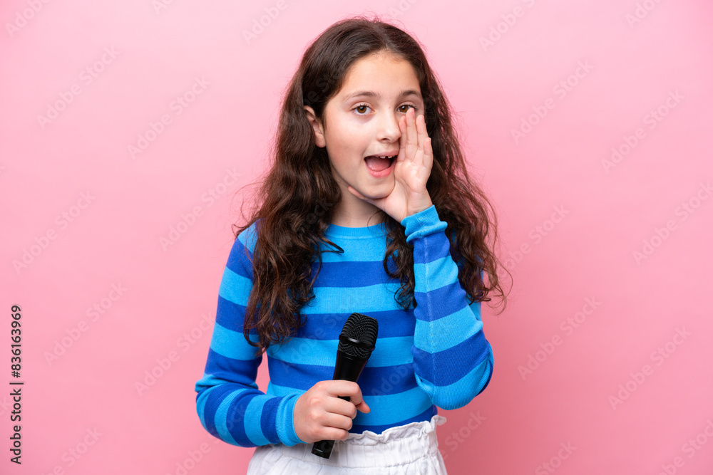 Little singer girl picking up a microphone isolated on pink background shouting with mouth wide open Little singer girl picking up a microphone isolated on pink background shouting with mouth wide open
