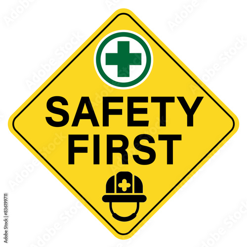 Safety first, diamond shape warning sign with text, green cross symbol and a hard hat silhouette below.