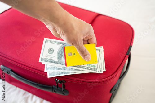 Unrecognizable businessman showing US dollars and yellow credit card on a red suitcase on a bed © cunaplus
