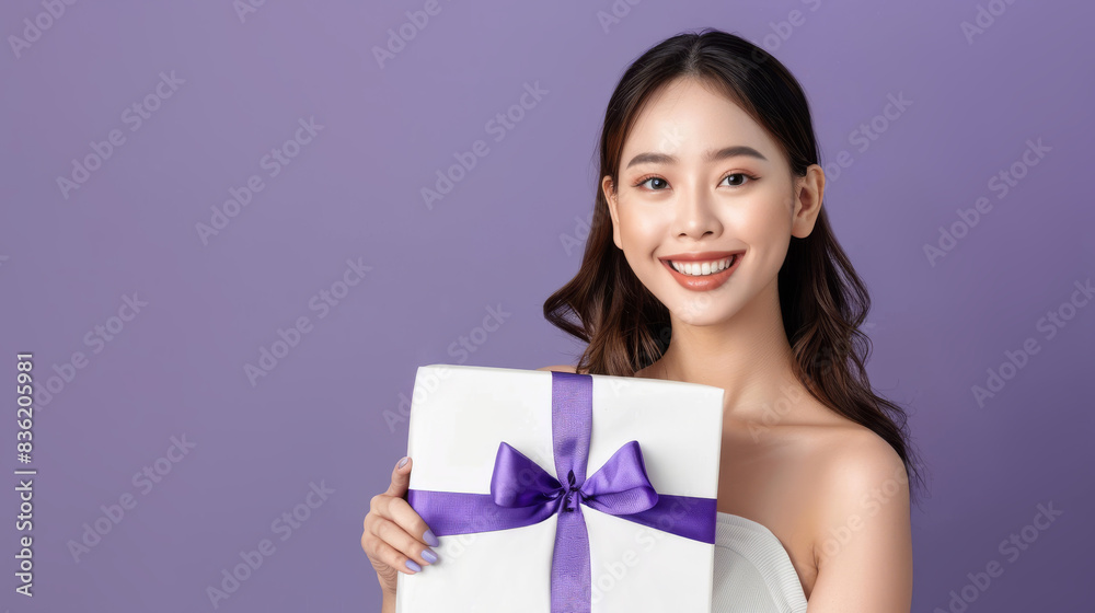 Asian woman is holding a white box with a purple bow on it Asian woman is holding a white box with a purple bow on it