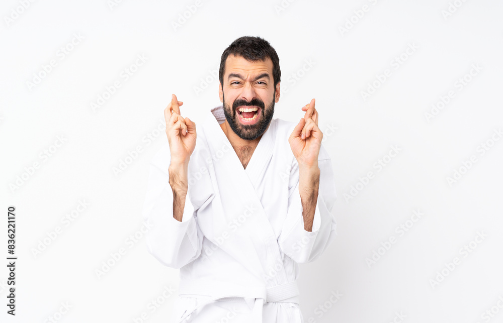 Young man doing karate over isolated white background with fingers crossing Young man doing karate over isolated white background with fingers crossing