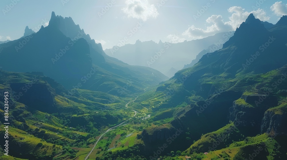 Fototapeta premium Sunlit green trees and rolling hills in a majestic mountain valley with clear skies above.