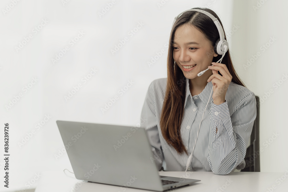Beautiful Asian female salesperson or call center operator wearing a wireless headset is talking with a customer on the phone. Provide advice and communicate with customers via computer video calls.
