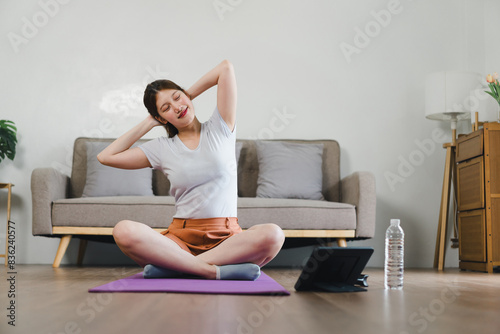 Young Asian woman at home doing exercise in front of open laptop, repeating instructions by professional online fitness trainer.