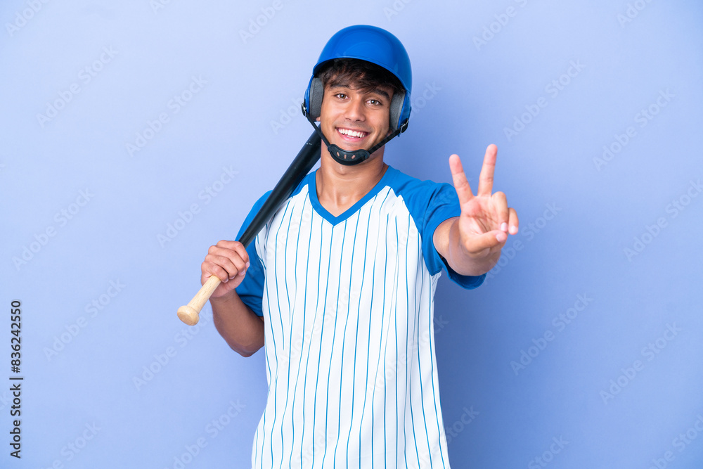 Baseball caucasian man player with helmet and bat isolated on blue background smiling and showing victory sign Baseball caucasian man player with helmet and bat isolated on blue background smiling and showing victory sign