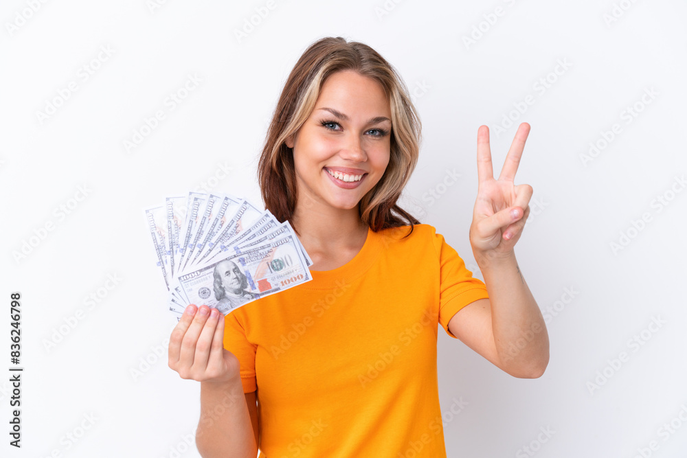 Young Russian girl holding dollars isolated on white background smiling and showing victory sign Young Russian girl holding dollars isolated on white background smiling and showing victory sign