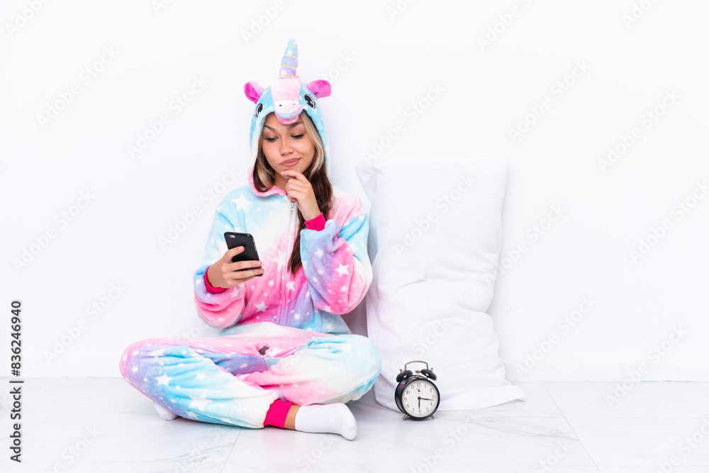 Young Russian girl wearing a unicorn pajama sitting on the floor isolated on white background thinking and sending a message Young Russian girl wearing a unicorn pajama sitting on the floor isolated on white background thinking and sending a message