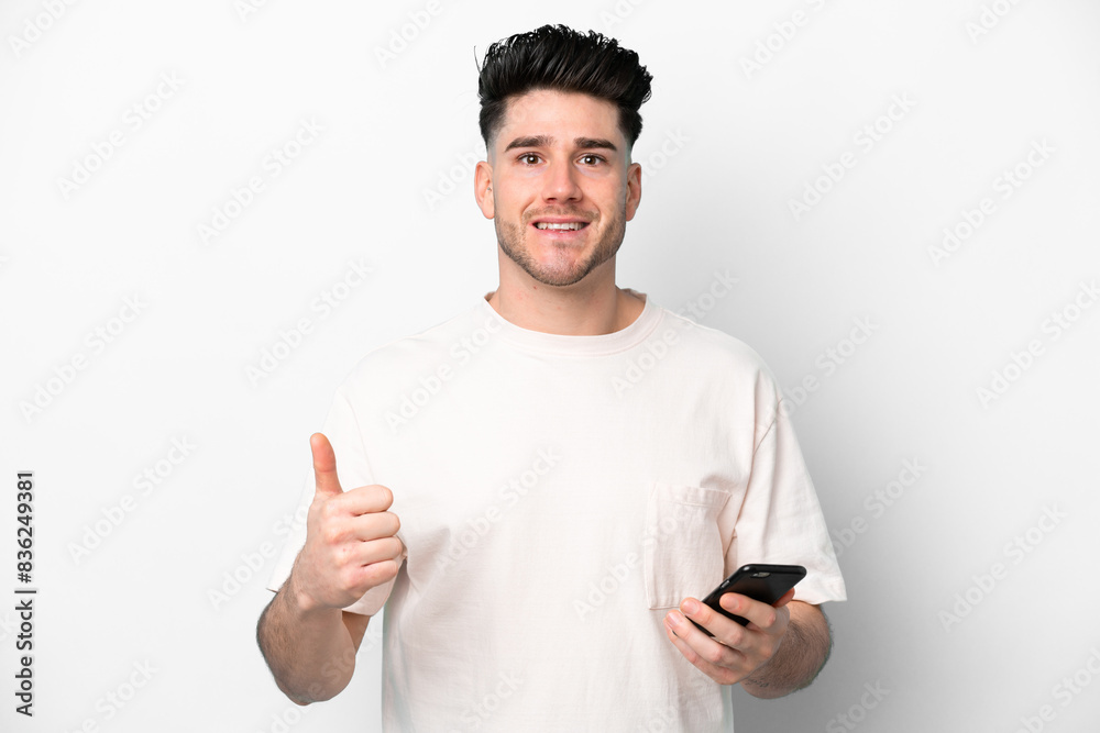 Young caucasian man isolated on white background using mobile phone while doing thumbs up Young caucasian man isolated on white background using mobile phone while doing thumbs up