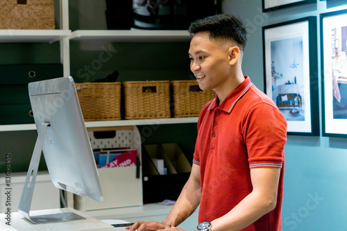 Smiling man looking at his computer desktop while standing in his working space. doing virtual meet through computer