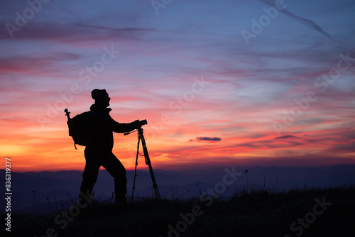 Silhouette of a photographer on top of a hill watching beautiful sunset. 