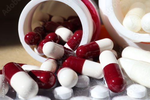 white or white medicine capsules and spilling out of container lying on the table photo