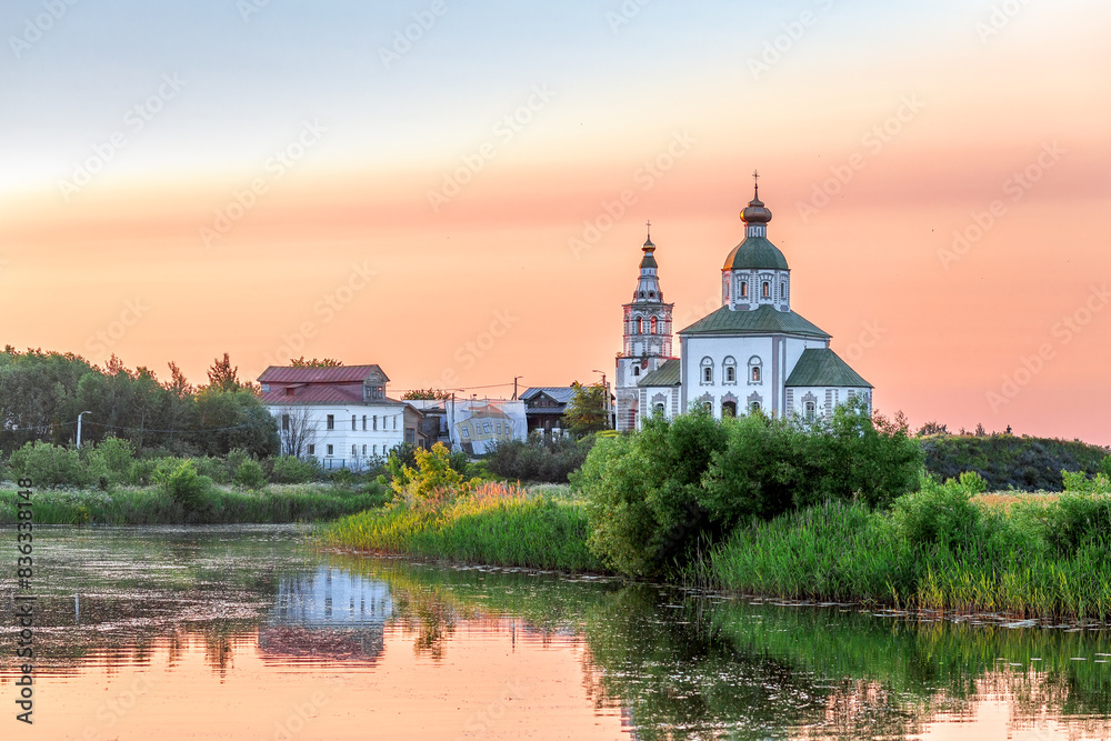 Fototapeta premium SUZDAL, RUSSIA - Beautiful landscape of Suzdal overlooking the Kamenka River and the ancient Russian Church of Elijah the Prophet (Ilyinsky Church)At sunset