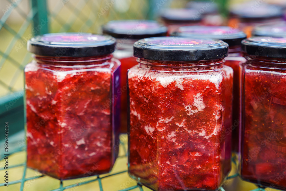 Fresh strawberry jam, preserved in jars, stands in a mesh metal box. Farm natural products. Conservation and preparations.