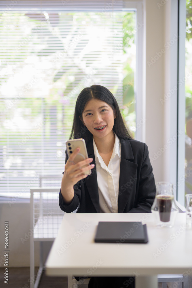 Obraz premium Professional businesswoman working on her smartphone in a bright, modern cafe with coffee and greenery