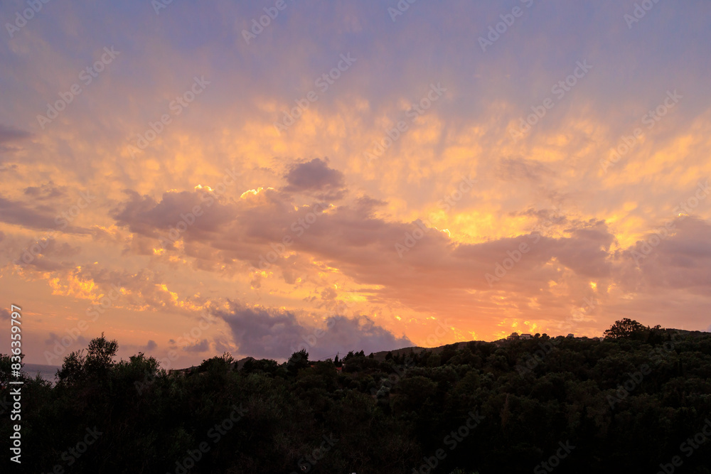 Colourful sunset in the bay of Agios Georgios with dark clouds in front of an intensely orange sky with individual strangely shaped dark wispy clouds on the island of Corfu