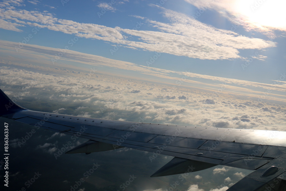 The wing of a jet plane and the scenery on the ground are visible through the porthole. The wing of a jet plane and the scenery on the ground are visible through the porthole.