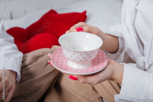 Female hands with long nails and bright manicure hold a white and pink tea pair with hearts