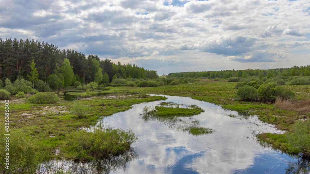 A serene pond sits peacefully in a vast field, with a charming house standing proudly in the background, creating a picturesque scene of tranquility A serene pond sits peacefully in a vast field, with a charming house standing proudly in the background, creating a picturesque scene of tranquility
