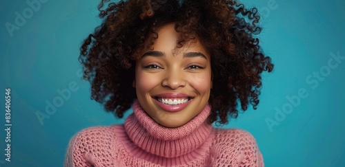 Woman With Curly Hair Smiling in Pink Sweater Against Blue Background