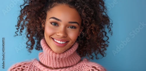 Woman With Curly Hair Smiling in Pink Sweater Against Blue Background