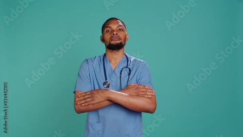 Portrait of serious professional male nurse standing with arms folded, studio background. Stern healthcare worker wearing protective clinical scrubs to prevent spreading of diseases, camera B photo